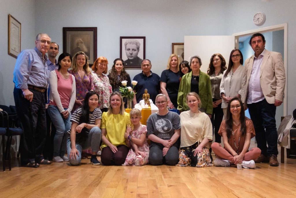 a diverse group of people facing the camera in two rows surrounding a statue of Buddha